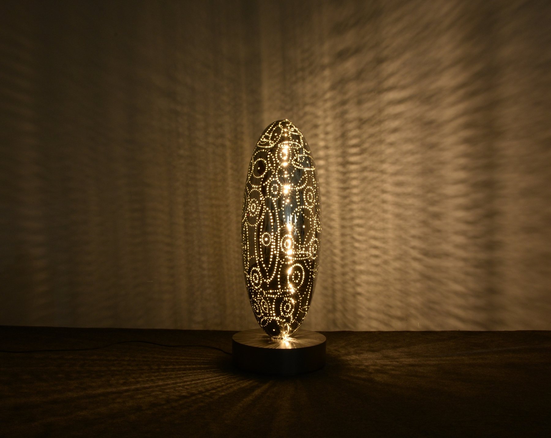 Illuminated oval sculpture casting a patterned shadow