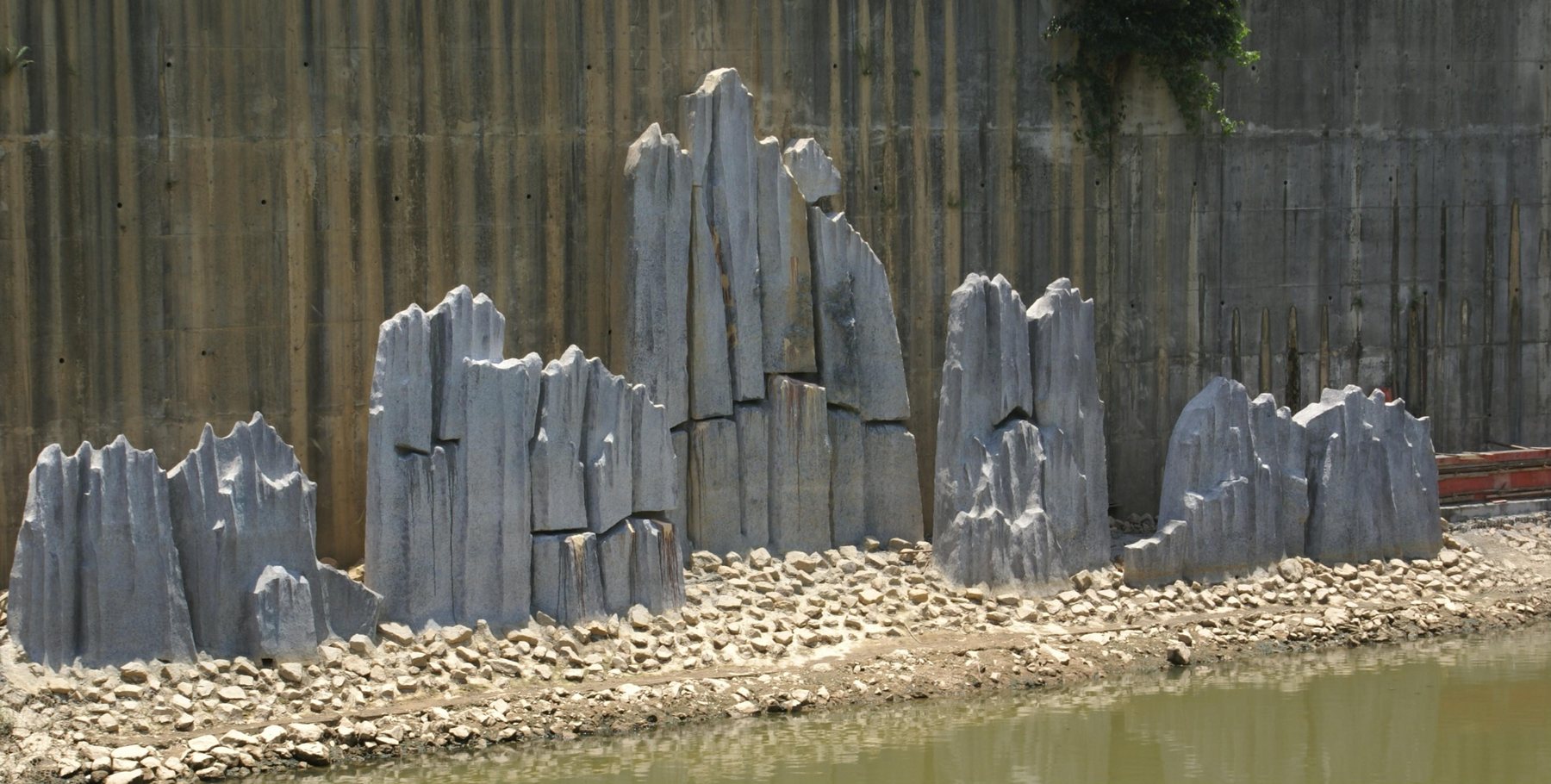 Grey mountain-like sculpture at a waterside landscape