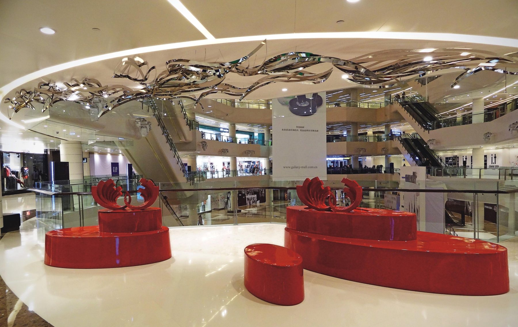 Suspended reflective forms above red sculptures in the mall atrium
